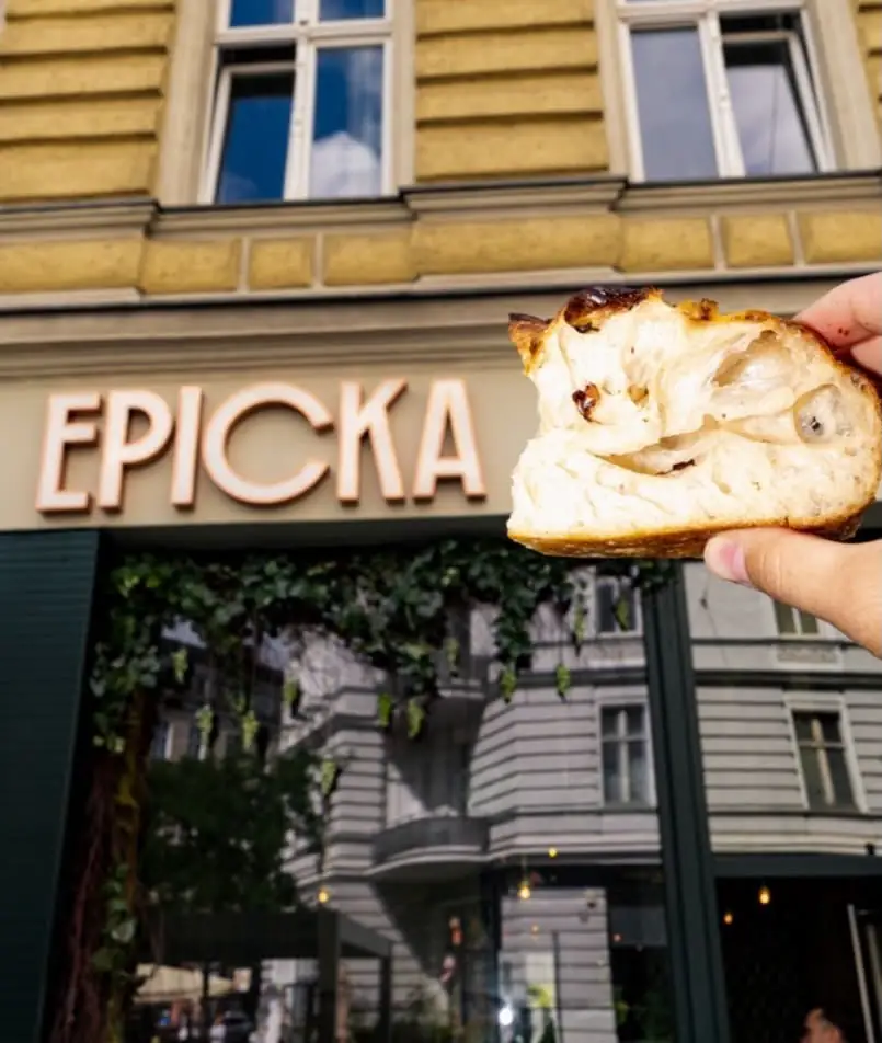 Szyld EPICKA nad witryną lokalu, na pierwszym planie ręka z kawałkiem pizzy